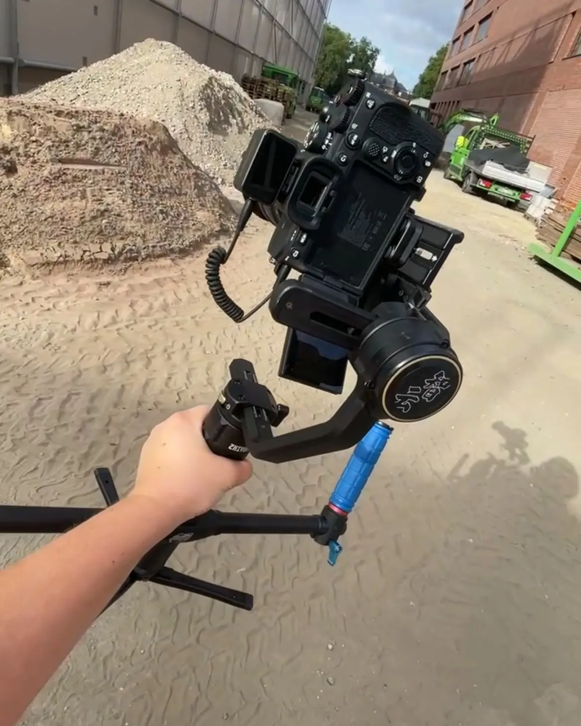Kamera auf dem Gimbal über der Baustelle, im Hintergrund Sandhaufen und ein Rohbau