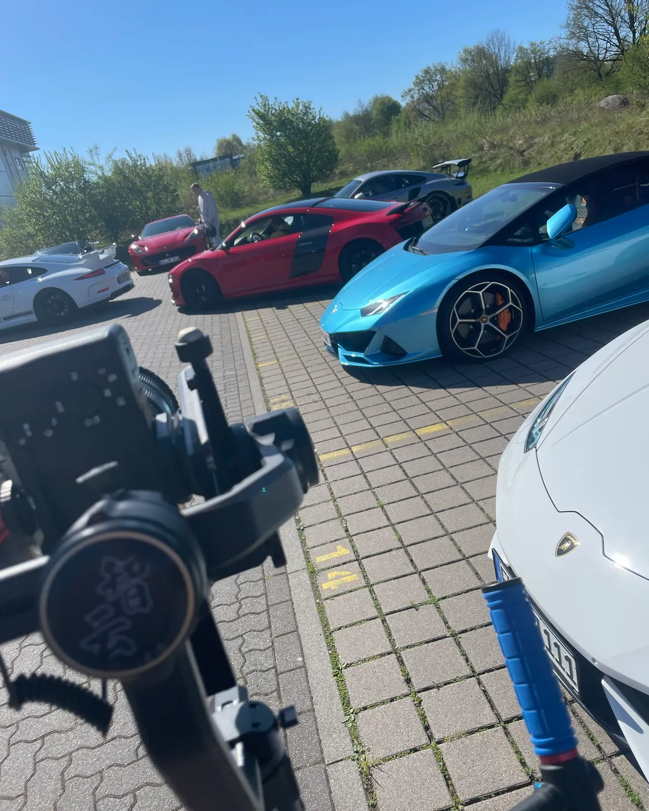 Gimbal im Vordergrund, dahinter ein blauer Lamborghini Huracán und weitere Sportwagen